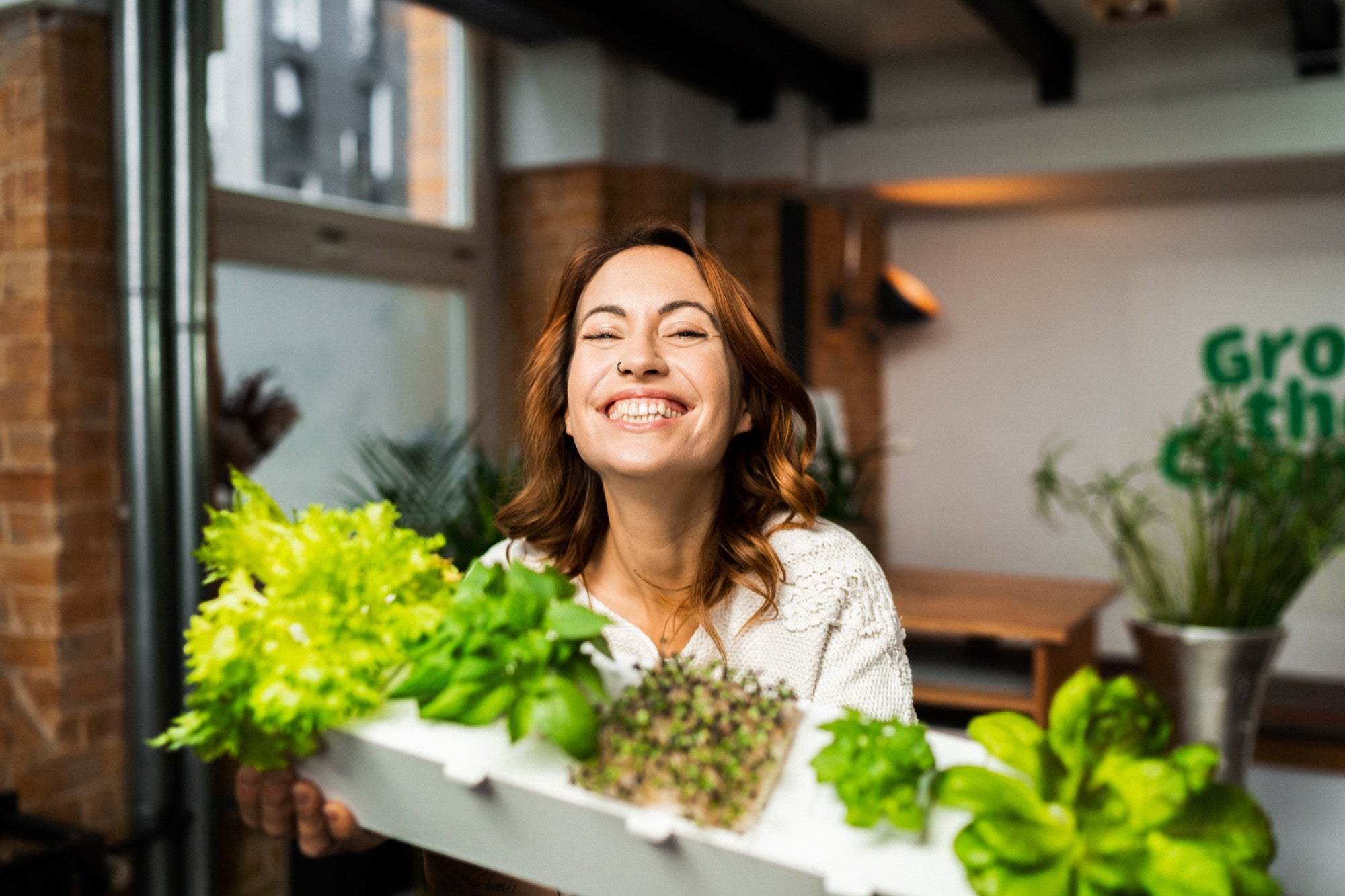 Frau ist stolz auf ihre selbst angebauten Kräuter und Salate, die sie im Indoor Garten homefarm von urbanhive angebaut hat.