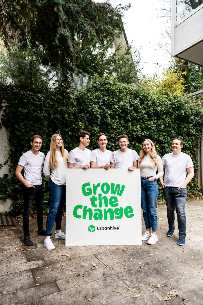 urbanhive Team mit einem großen Plakat mit dem Schriftzug Grow the change, der auf die Vorteile und die Frische beim eigenen Anbau mit dem Indoor Garten homefarm hinweisen soll.