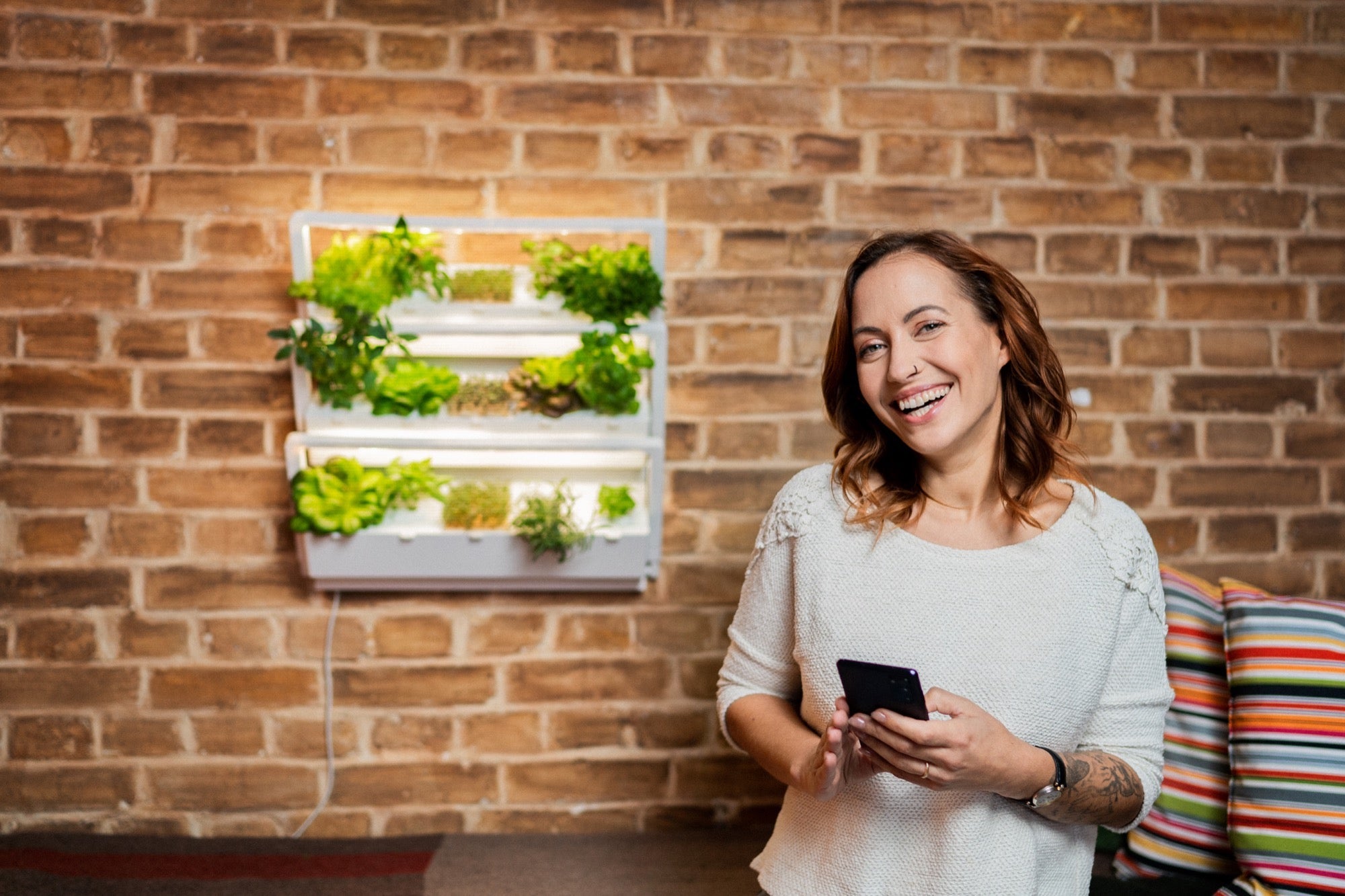 Frau steuert ihren indoor garten homefarm hanz einfach über android oder ios Smartphone und kann so ihre frischen Pflanzen beim Wachsen überwachen