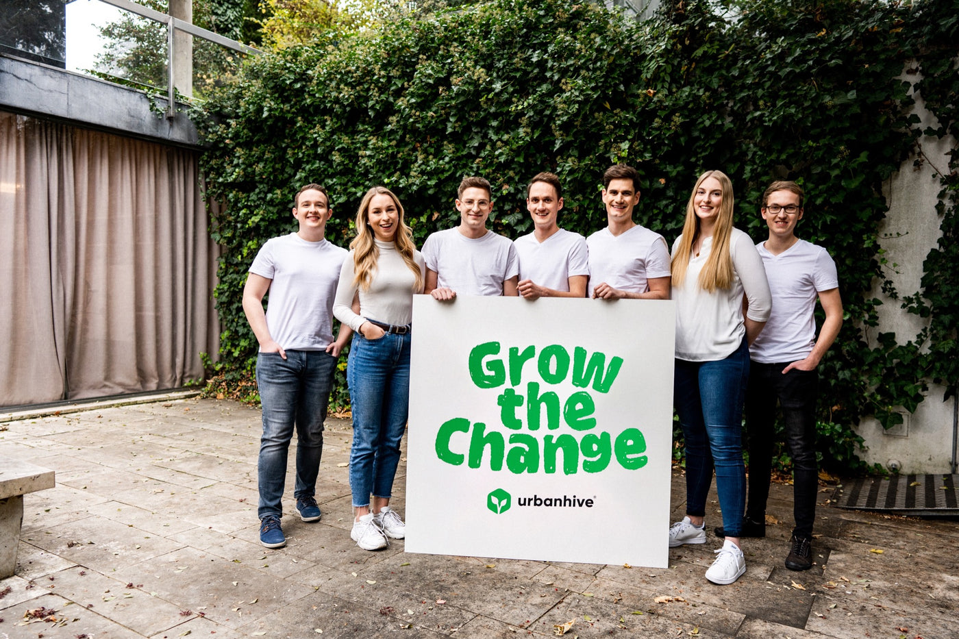 urbanhive Team mit einem großen Plakat mit dem Schriftzug Grow the change, der auf die Vorteile und die Frische beim eigenen Anbau mit dem Indoor Garten homefarm hinweisen soll.